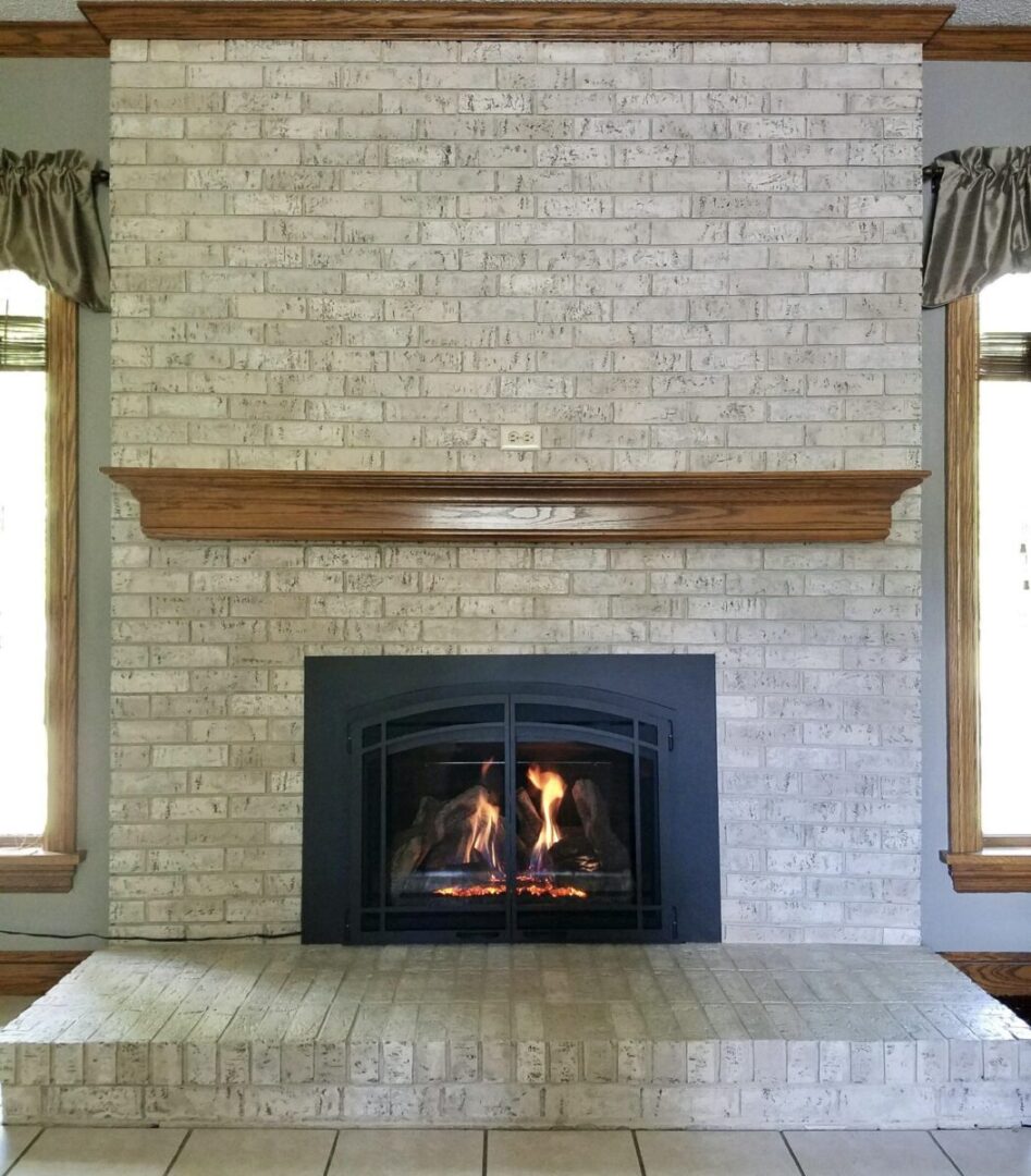 A gray painted brick fireplace with black fireplace doors, which stretches from the ceiling to the floor.