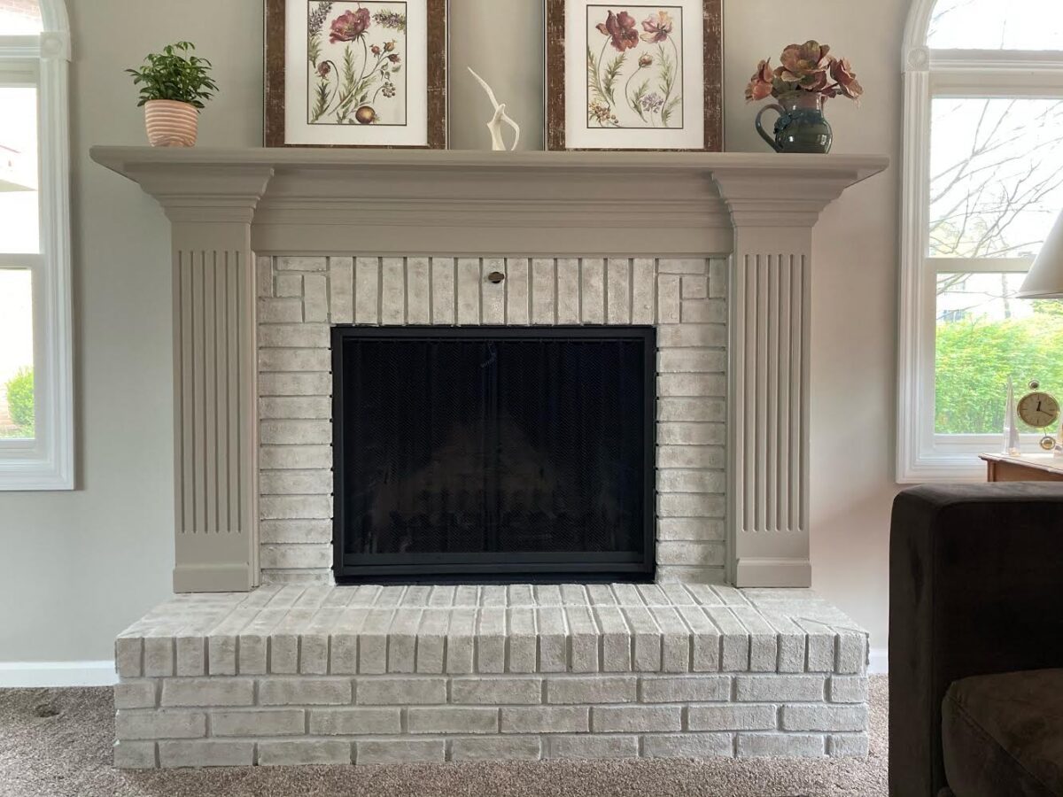 A gray painted brick fireplace with flowers and art on the mantel.